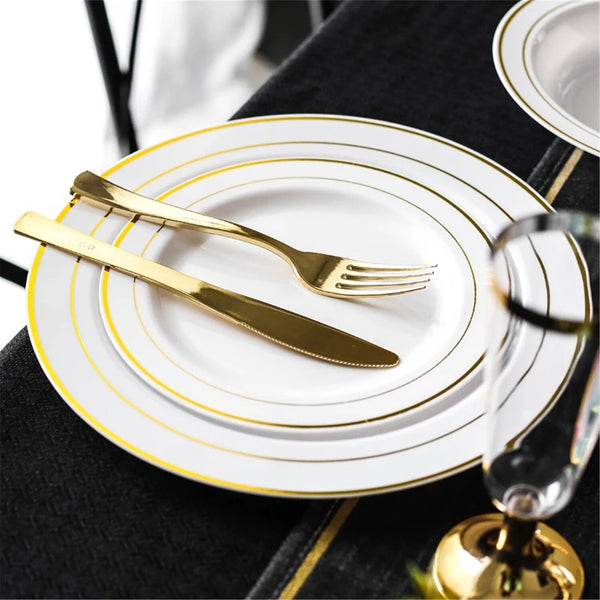 Gold rimmed plastic plate with gold fork and knife on a dark table