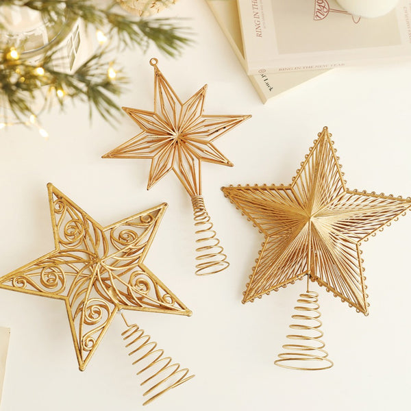 Three gold star tree toppers laid on a table with greenery