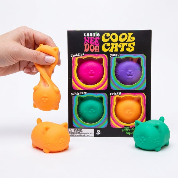Hand stretching an orange squishy cat beside the box and a green cat