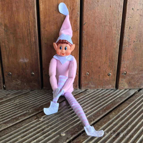 Pink boy Christmas elf doll sitting on a timber deck