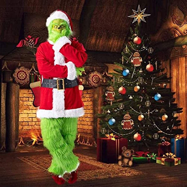 Man in the green grump Santa suit beside a decorated Christmas tree and fireplace